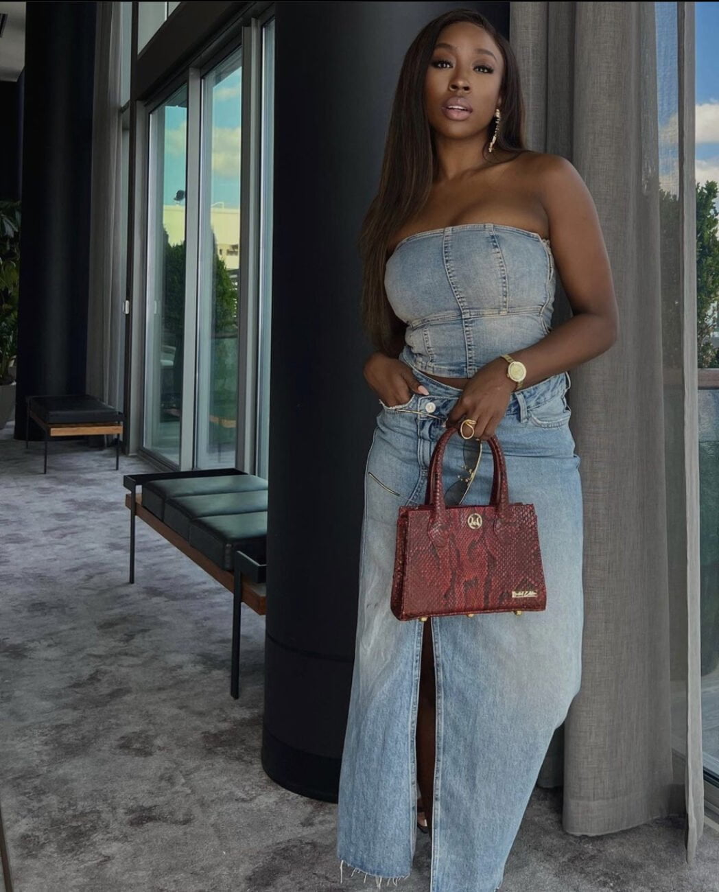 Slaying in denim again: Beverly Naya pairs a sleeveless denim top with a maxi  skirt and adds a pop of red with a handbag.