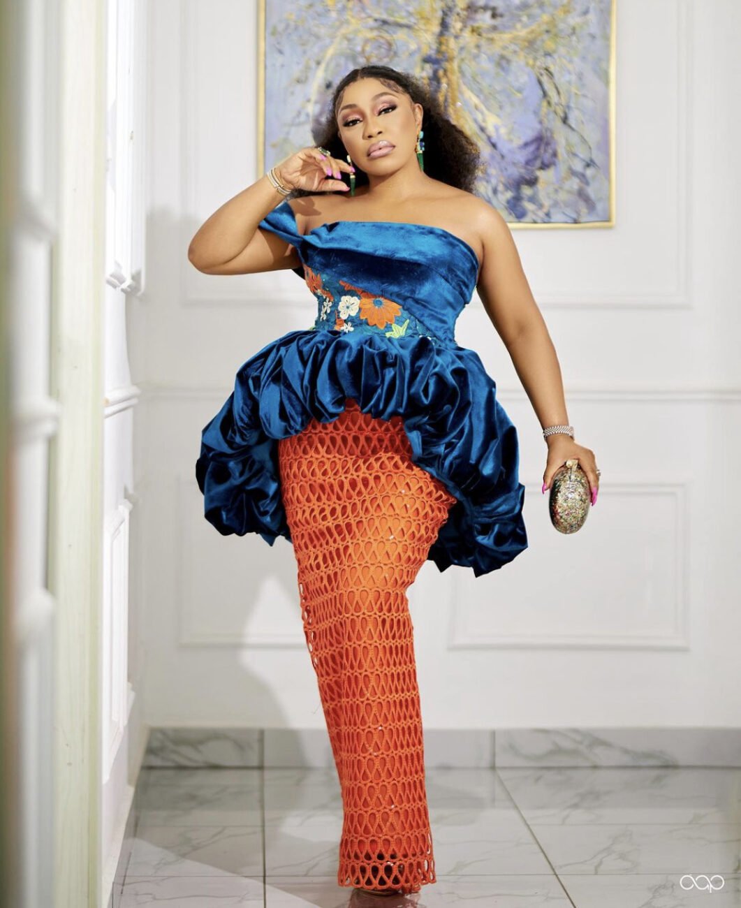 Rita Dominic in a blue suede top and orange lace skirt, showcasing fashion brilliance.