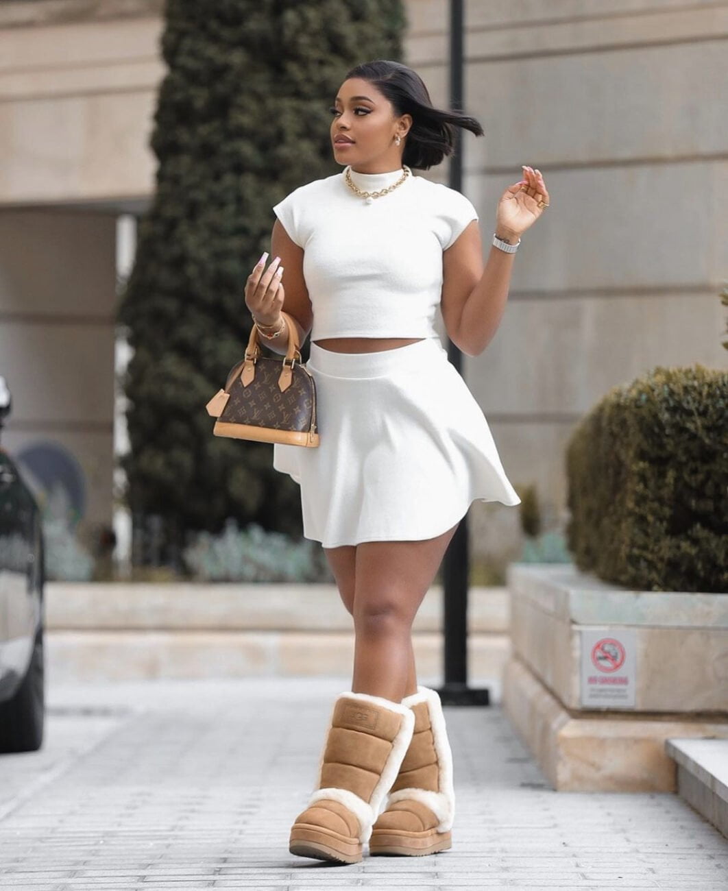 White pleated skirt paired with a white crop top, brown fur boots and a brown handbag.