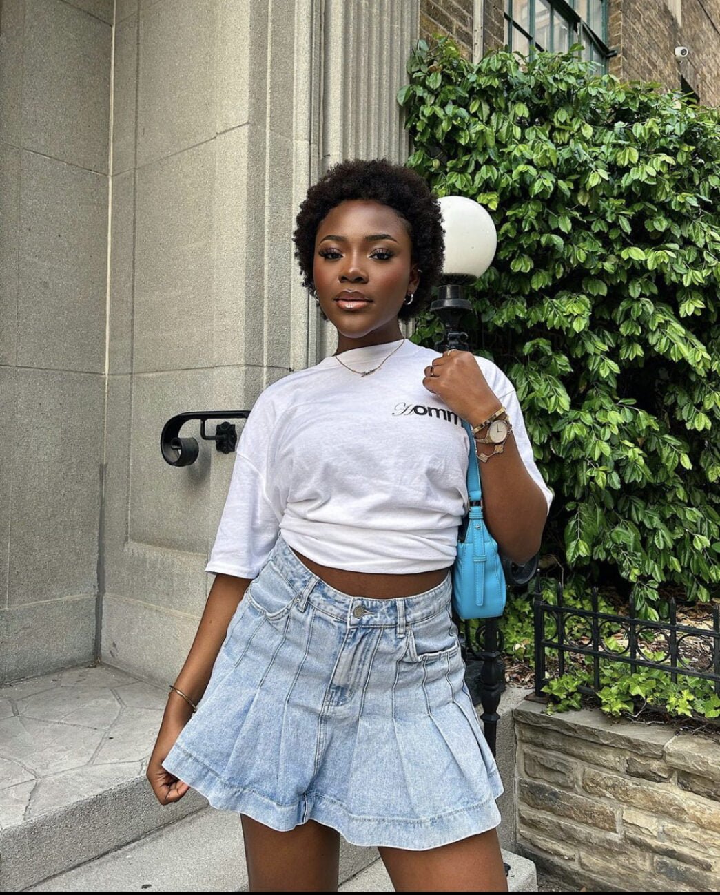 Pleated denim skirt paired with a white crop top and a blue handbag. 