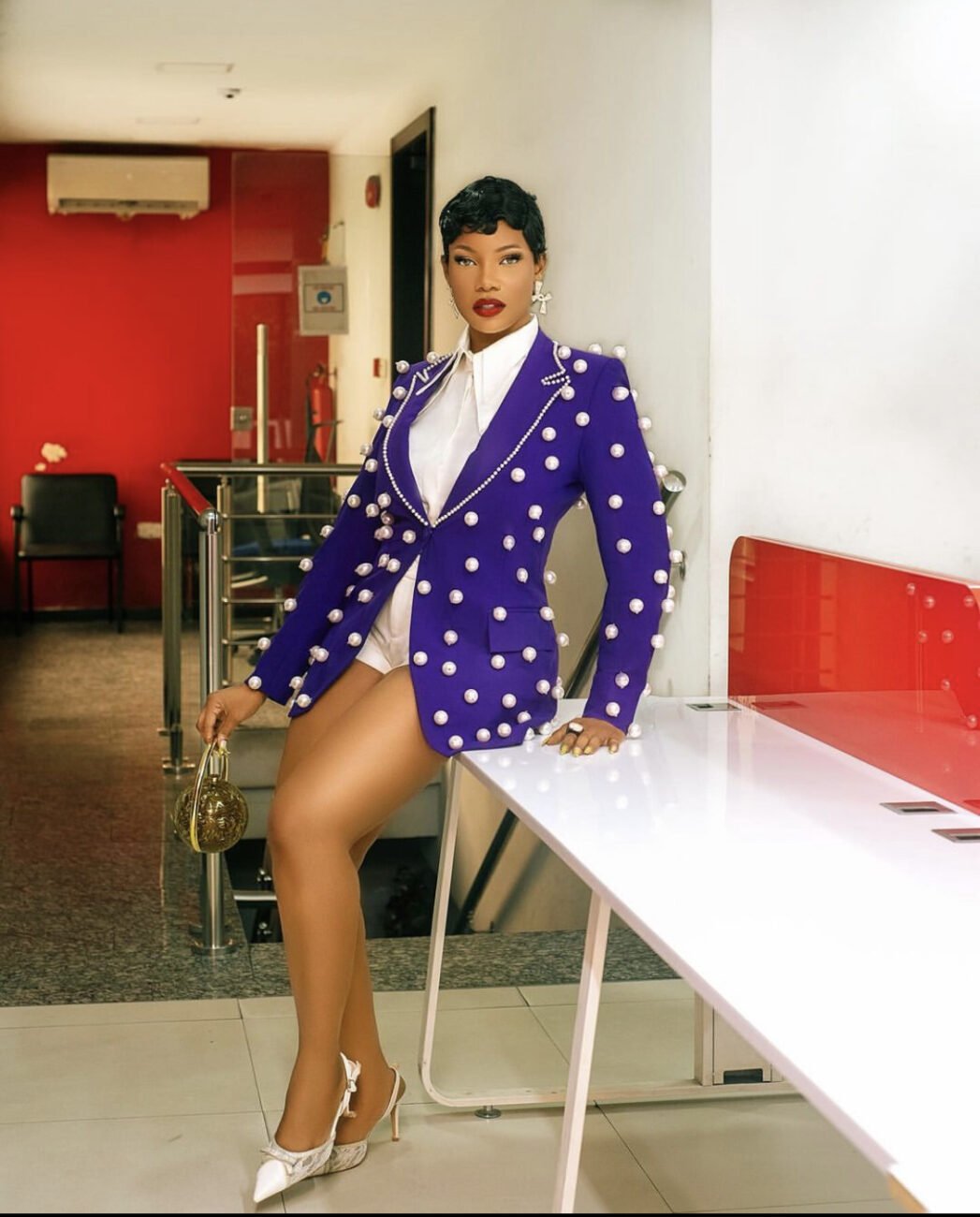 Tacha in a purple suit with white beads attached all over it, paired with a white collared shirt and mini white shorts.