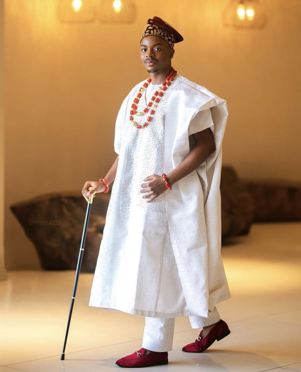 Enioluwa Adeoluwa in an ‘Agbada’ with red shoes, red beads, and a blue walking stick.