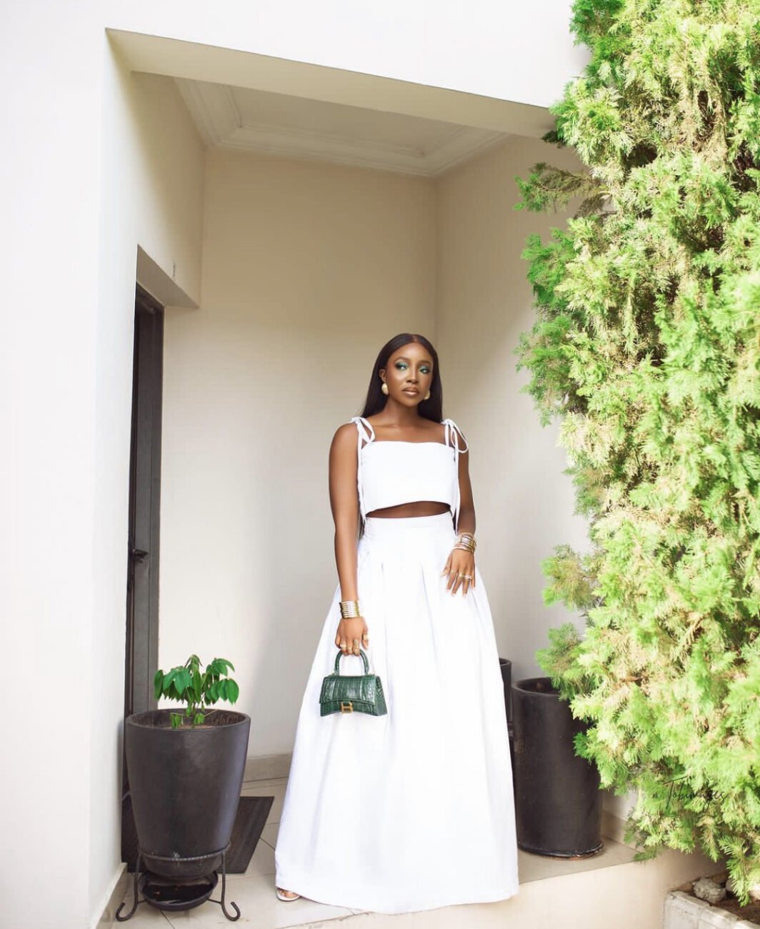 Ini Dima-Okojie in a white two-piece, with a green purse.