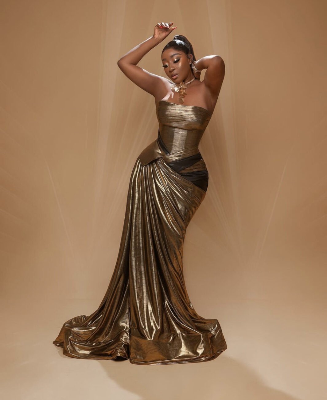 Ini Edo in a sleeveless bronze dress that matches her skin tone.