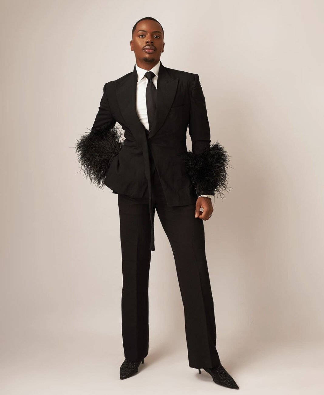 Enioluwa Adeoluwa in a black suit with feather covered sleeves.