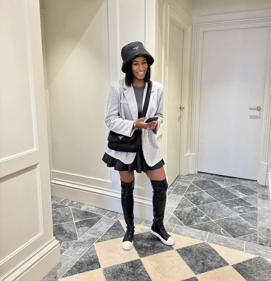 Dj Cuppy in a grey sweater jacket, a grey top, and a black skirt, which was paired with black boots.